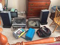 Full view of stereo system components including speakers and turntables with cassette tapes and accessories on carpeted floor.