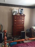 Full height view of wooden chest of drawers dresser with brass handles and decorative top drawer. Visible items on top are not included.