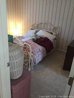 Side view of white metal bed frame with brass accents, pillows, linens, and baskets next to bed