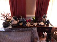 Table with various ceramic and glass decorative items including a pagoda birdhouse, a large chickadee bird figure, a pink flowering bonsai tree, glass bowls and small ceramic pieces