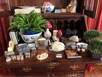 Wide view of all items arranged on wooden surface showing miniature buildings, dishes, dog figurines, plants, decorative hearts and floral items