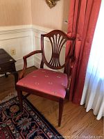 Wooden armchair with pink upholstered seat and carved backrest in a room corner next to a window with curtains.