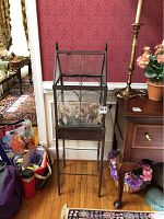 Front view of metal and glass terrarium on stand showing dried leaves inside and the overall shape.