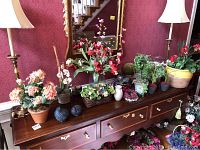 Wide view of console table with many faux flower arrangements, metal partridge figurines, Williamsburg pottery vase, pillar candle in glass, large ceramic pot, and silk flowers arranged underneath a large mirror, flanked by two lamps (not included).