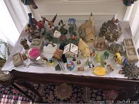 View of varied bird figurines, miniature cottages, and mixed small decorative objects arranged on a table.