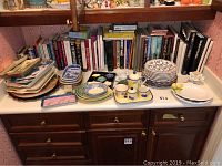 Wide photo of all dishes and ceramic items arranged on counter including books behind