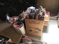 Photo shows several cardboard boxes and bags containing many rolls of Christmas wrapping paper, upright in a large moving box.