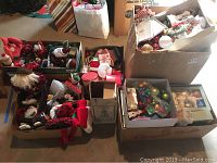 Photo showing several boxes filled with assorted Christmas ornaments, Santa figurines, plush decorations, and candles on the floor.