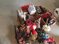 Photo shows multiple cardboard boxes filled with Christmas decorations and statuaries arranged on a concrete floor. Items include artificial flowers, Santa and snowman figurines, decorative cones, wreaths, and garland.