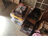 Boxes with various cassette tapes and CDs stacked on top of plastic containers, showing quantity and general condition.