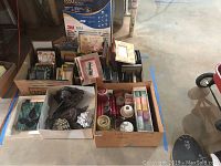 Multiple boxes containing assorted picture frames, candles, and small items viewed from above on cement floor