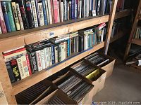 Large wooden shelves with mixed fiction and non-fiction books arranged in rows and boxes with vinyl records below