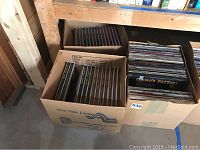 Two boxes under shelf: left contains hardcover art books, right contains vinyl records