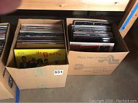 Two cardboard boxes filled with assorted 12-inch vinyl LP records on a shelf