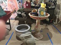 Wide shot of the ceramic bird bath on mosaic pedestal alongside gray planter and rabbit statue in the foreground.