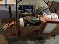 Photo showing boxed kitchenware items including wooden utensils, cooking utensils, dish racks, and various pots and pans in cardboard boxes and shelving units