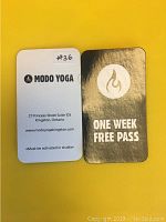 Front and back of Modo Yoga one-week free pass cards. White front with address and branding; black and gold back with flame logo and 'One Week Free Pass' text.