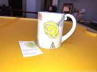 Full side view of the mug and a business card showing the brand and artist.