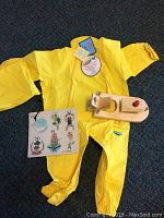 Photo of a bright yellow Splashy waterproof rain suit, a wooden toy boat with red and round porthole details, and Londji pirate themed magnets on a magnetic sheet.