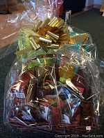 Full view of the wrapped gift basket showing packaging, assortment of items inside, and decorative gold bow on top.