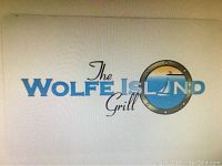 Photo of a white card showing The Wolfe Island Grill logo with blue letters and a sailboat inside a porthole illustration.