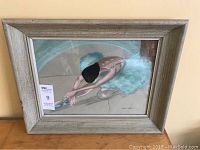 Framed pastel artwork of ballet dancer stretching, showing full piece in light wooden frame on a wooden surface.