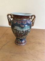 Front view of the hand painted Asian pottery vase showing detailed artwork with people riding horses and gold-colored handles.