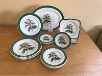 Full overview of the part dinnerware set showing plates and platters with green rim and botanical Peggy O'Neill design.