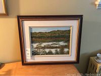 Photo shows the full framed oil painting of a Canadian landscape placed on a surface against a wall.