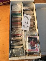 Box filled with a large quantity of assorted sports cards organized in six sections separated by cardboard dividers, cards mostly contained in transparent plastic protective sleeves.