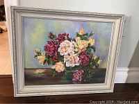 Full frontal view of the signed floral painting by Baker in a white frame showing the arrangement of pink, purple, yellow, and cream roses in a glass vase on a table with a soft shaded background.