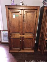 Front view of a medium brown wood cabinet with four paneled doors and round knobs, showing minor wear to finish and slight surface damage.