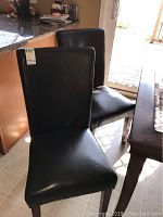 Two of the four black high back armless chairs shown near a kitchen counter. Chairs are upholstered in worn black material with some fabric separation.