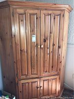 Front view of pine wood cabinet showing closed upper double doors with paneled design and round wooden knobs.