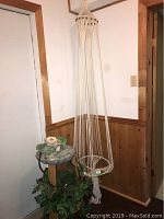 Macrame hanging plant holder displayed standing against wall, showing long cream cords, ring for attaching and fringe at bottom.