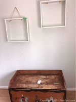 Wooden chest with painted horsemen in front and worn surface top, two empty white wall shelves above it