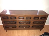 Front view of wooden dresser showing all nine drawers and brass/wooden handles with visible wear.