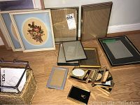 Multiple small brass frames and larger frames with floral prints and neutral tone frames on floor