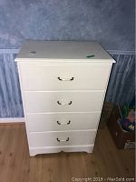 Front view of white wooden dresser with four drawers and metal handles against blue wall and wooden floor.