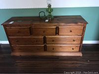 Front view of the wooden dresser showing all 7 drawers with round metal knobs and a natural wood finish.