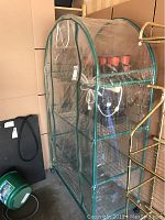 Full view of portable greenhouse frame with plastic cover and zippered door, shelves inside visible