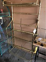 Full view of brass baker's rack showing four wire shelves and brass frame.