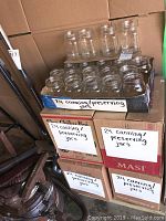 Five boxes each labeled '24 canning/preserving jars' stacked, some jars outside boxes. Jars clear glass no lids.