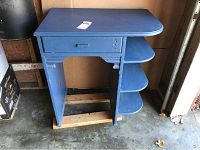 Blue wooden desk with one drawer and three curved shelves on right side, showing front view.