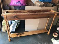 View of the full rectangular wooden planter with turned legs and lower shelf.