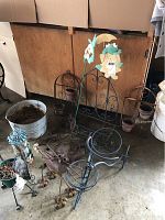 Wide view showing multiple metal garden ornaments on concrete floor near wood wall. Includes bear-shaped wind chime, metal bucket, and plant hangers with attached pots.