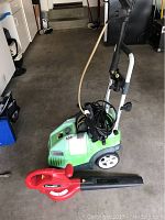 Greenworks pressure washer with hose and wheels along with red Homelite leaf blower on concrete floor