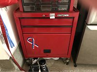 Front view of red metal Craftsman tool bench showing two drawers and one bottom cabinet section with caster wheels visible.