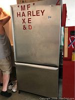 Full front view of Amana stainless steel refrigerator freezer with some letters attached to fridge door.