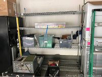 Front view of the metal rack showing four wire shelves containing several storage bins (not included in the lot). Rack mounted on wheels with brakes visible.